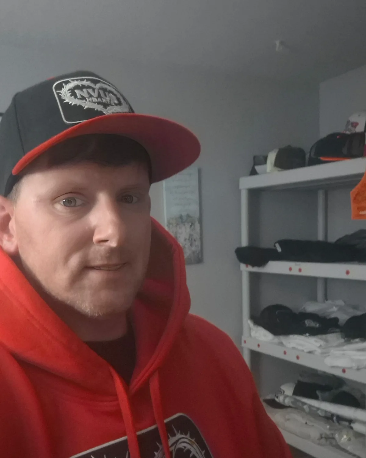 Keith, founder of NVUS Hearts, wearing a red NVUS Hearts hoodie and cap in the brand's stockroom