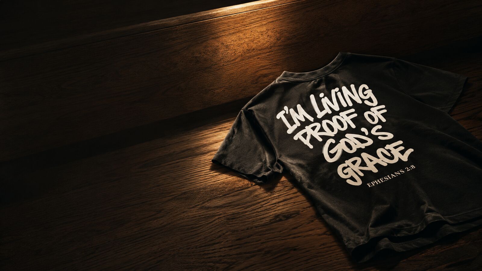 Black Living Proof of God's Grace tee resting on a dark church pew in warm light, Ephesians 2:8